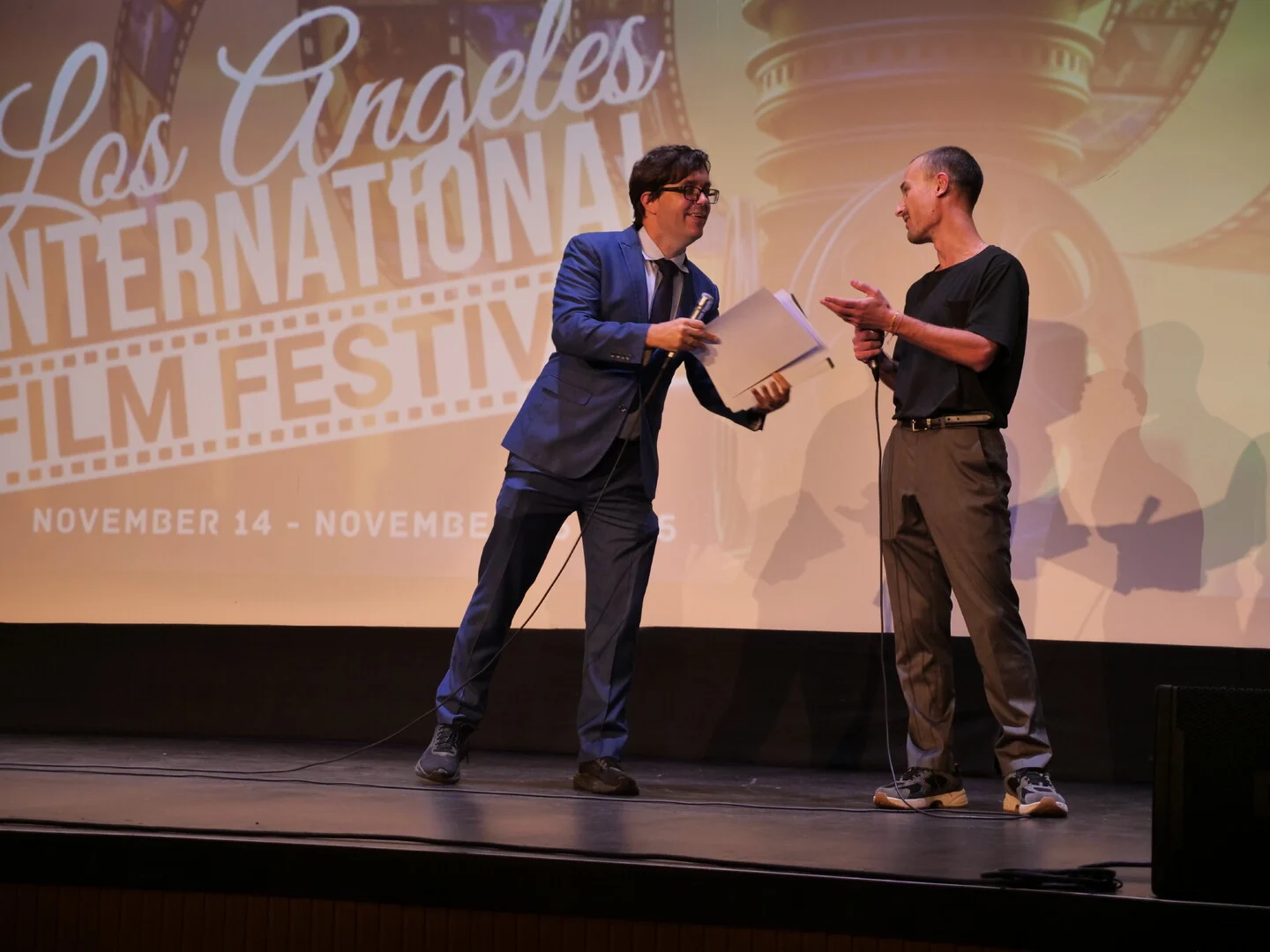 Two speakers exchanging a programme on the LAIFF stage